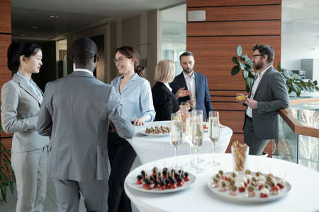 Two groups of successful speakers in formalwear talking by served tables during buffet in luxurious restaurant in business centerの写真素材