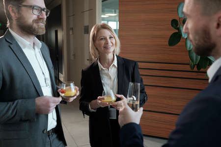 Group of contemporary entrepreneurs with juice looking at colleague with flute of champagne making toast for business at buffetの写真素材
