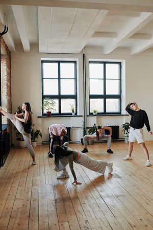 Group of adolescent people in activewear doing warmup exercises on wooden floor of dance hall or studio of modern dancingの写真素材