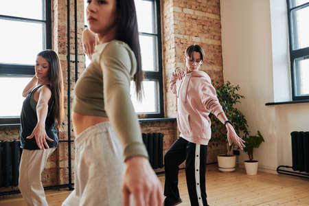 Group of contemporary teenage girls and guy in activewear practicing vogue dance movements during training in loft studioの写真素材