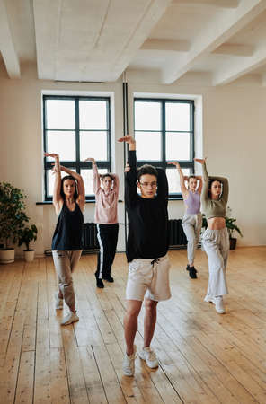 Young teenage male leader of performance group showing vogue dance exercises to group of girls and guy during training in studioの写真素材