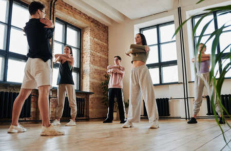 Group of teenage performers in activewear repeating vogue dancing exercises after male instructor...