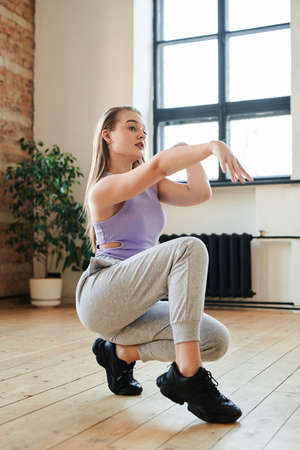Cute dynamic teenage girl stretching arm in front of herself during exercise or movement of vogue dance in loft studioの写真素材
