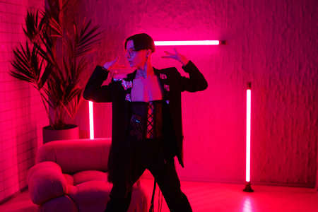 Contemporary young dancer in smart attire performing vogue dance in night club while standing in...