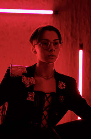 Low key image of young serious man in eyeglasses and smart apparel sitting in night club in front of...