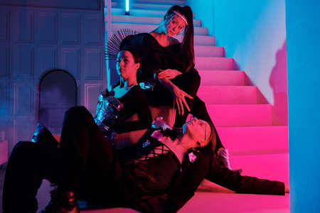 Posh teenage guy and two glamorous girls in stylish apparel relaxing on staircase in modern studio...