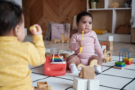 Over-the-shoulder shot of two lovely twin babies sitting on floor in living room playing with toysの写真素材