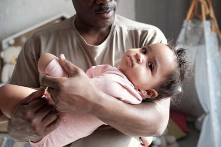 Medium close-up of loving African American father holding his baby daughter in arms lulling herの写真素材