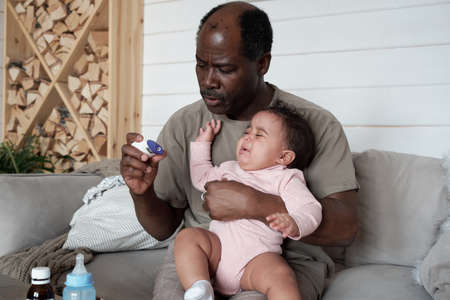 Horizontal medium portrait of mature African American man checking body temperature of his baby daughter with common coldの写真素材