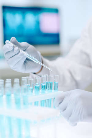 Contemporary chemist or researcher in gloves mixing two liquid substances while dropping one of them...