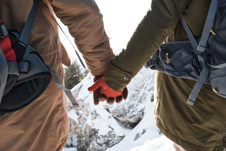 Medium close-up of unrecognizable active young man and woman in love standing on mountain top holding handsの写真素材