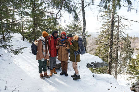 High angle view wide shot of young multi-ethnic friends hiking together in mountains choosing route...