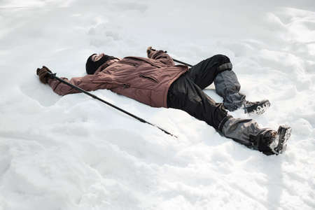 High angle shot of young guy wearing balaclava holding trekking poles relaxing on snowdrift on sunny...