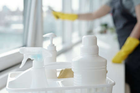 Three plastic bottles containing detergents for washing windows on sill against young worker of...