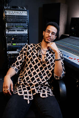 Portrait of stylish young Black man working in recording studio sitting relaxed looking at camera