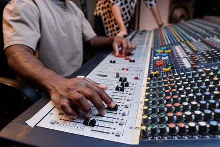Unrecognizable audio engineer and musician creating track using mixer in recording studio