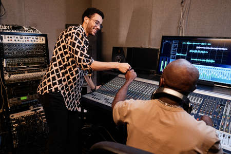 Successful African American music producer and young singer finishing work on song track in...