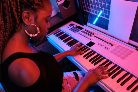 High angle shot of professional young African American musician playing digital keyboard in recording studio, neon lightの写真素材