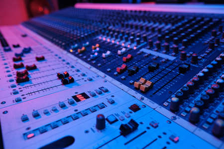 Horizontal no people shot of modern mixing console surface in recording studio in neon light