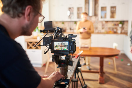 Young male videographer standing by video camera while shooting advertisement of cooking or...
