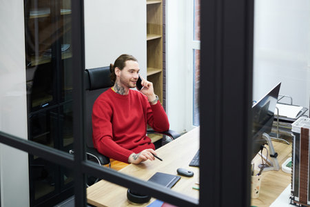 Smiling manager sitting at table at office in front of computer monitor and having business...