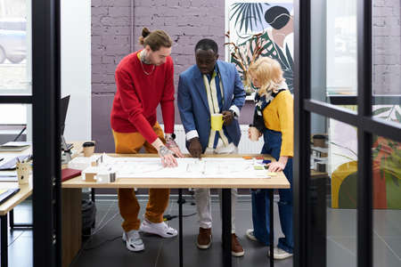 Group of architects standing at table and working over blueprint in team, they discussing new...