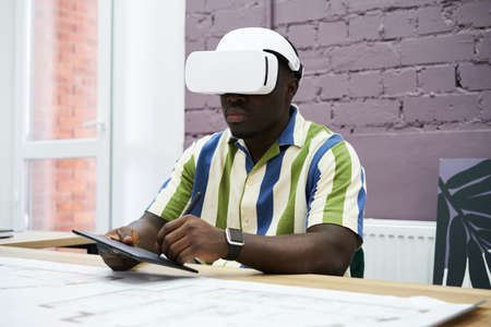 African young designer working in virtual reality headset at his workplace at officeの写真素材