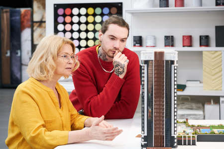 Architects looking at model of new building and discussing it at table during teamwork at officeの写真素材
