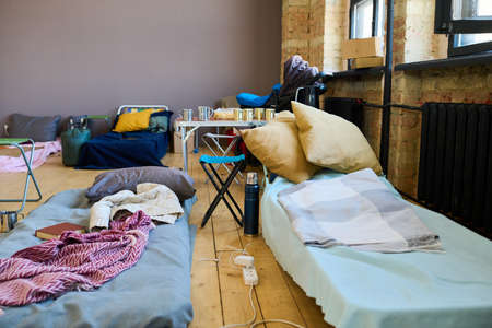 Two sleeping places of refugees with mattresses done with blankets or plaids in spacious room...