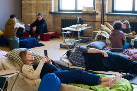 Young pregnant woman with smartphone texting or video chatting while lying on sleeping place xonsisting on mattress, plaid and pillowの写真素材