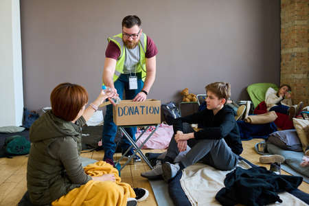 Pre-teenage boy looking at young female refugee taking bottle of water from hand of male volunteer...