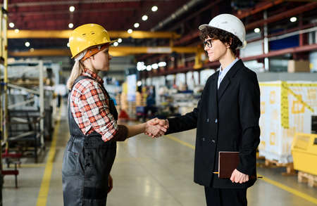 Two engineers of large modern factory shaking hands after discussion of terms of new project and...