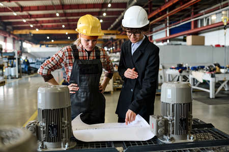 One of factory workers pointing at sketch on blueprint during explanation of sketch of new product...