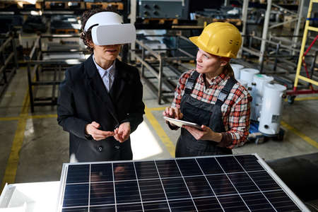 Two young engineers of factory discussing virtual model of new product while one of them using...