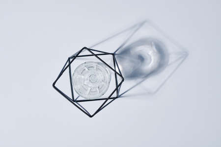 Flatlay of metal wire handmade holder with glass of water inside and its shadow on table or pastel grey background with copyspace aroundの写真素材