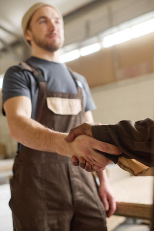 Young manual worker in overalls greeting his colleague at work shaking his handの写真素材