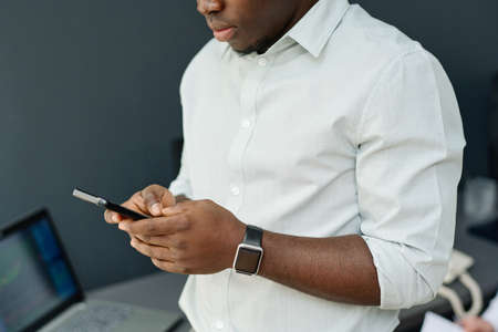 Portrait of young Black brokerage worker wearing white shirt watching data on smartphone in Internetの写真素材