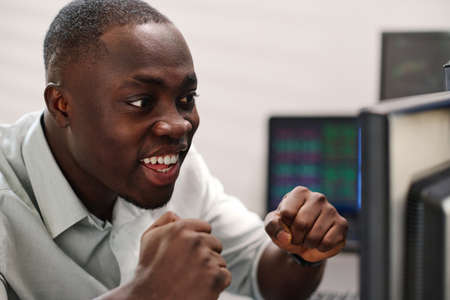 Close-up of cheerful African American man in formalwear looking at computer screen watching stock...