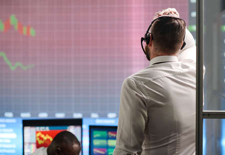 Unrecognizable Caucasian man wearing white shirt working in stock trading company looking at graph...