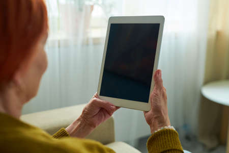Close-up of elderly woman holding touchpad in front of her face and talking online with her grandchildrenの写真素材