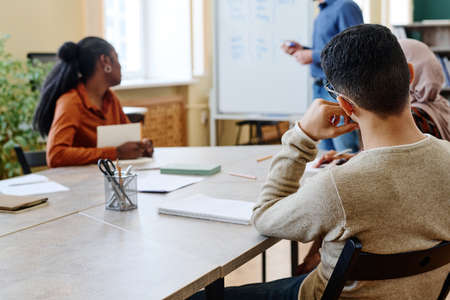 Unrecognizable multi-ethnic man and women sitting at table listening to teacher during English lessonの写真素材