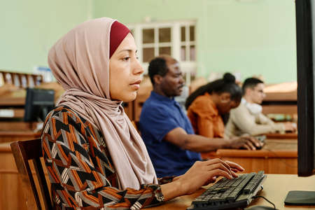 Young adult Middle Eastern woman wearing hijab working on computer in university libraryの写真素材