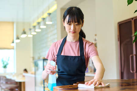 Female restaurant employee wiping the dining table in preparation to welcome customersの写真素材