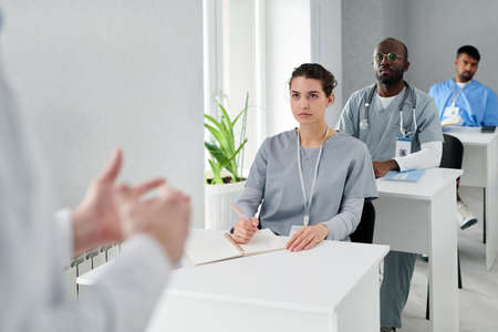 Group of physicians sitting at desk and listening to speaker during medical training at classの写真素材