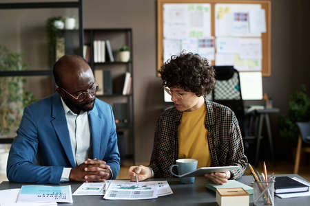 Businesswoman discussing financial graphs on papers with her partner at table during meeting