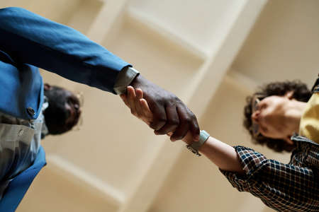 Low angle view of two multiethnic colleagues shaking hands to each other during meeting at office