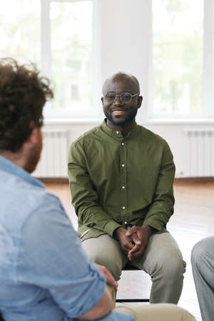 Happy young black man looking at another male describing his problem while both attending...