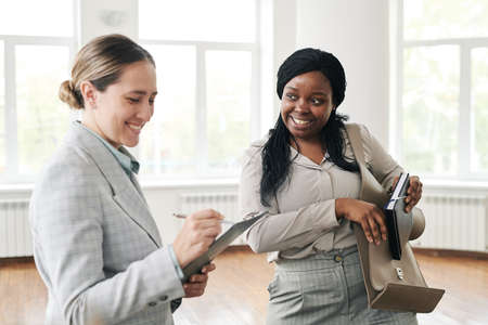 Two young interculltural females in formalwear having talk before psychological session while one of them pointing at documentの写真素材