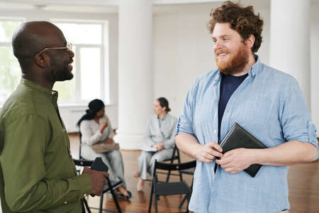 Happy young interracial men in casualwear having discussion against females communicating before or...