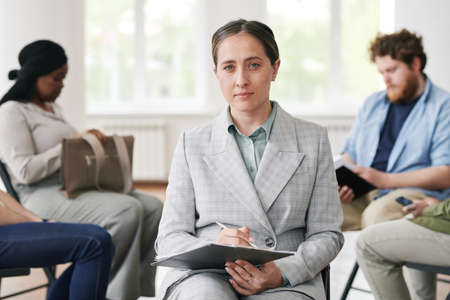 Young confident female counselor in elegant grey suit holding document while sitting in front of her...